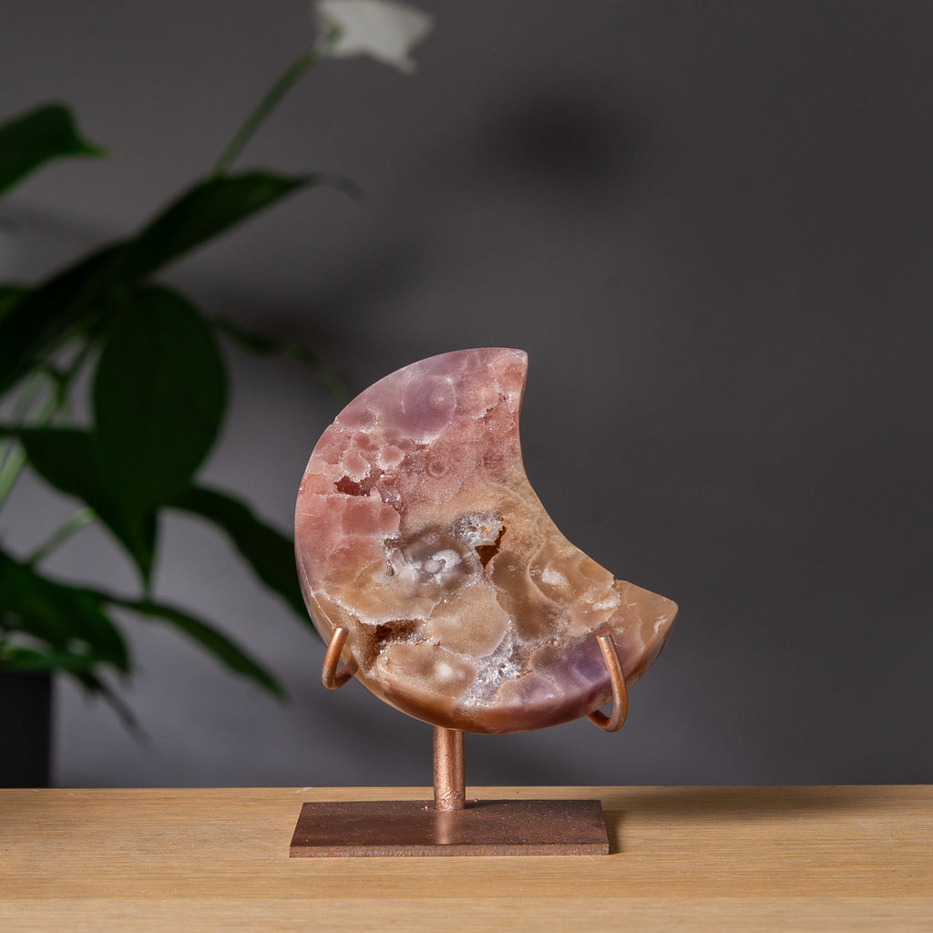 Månformad rosa ametist på stativ i mjuka pastelltoner